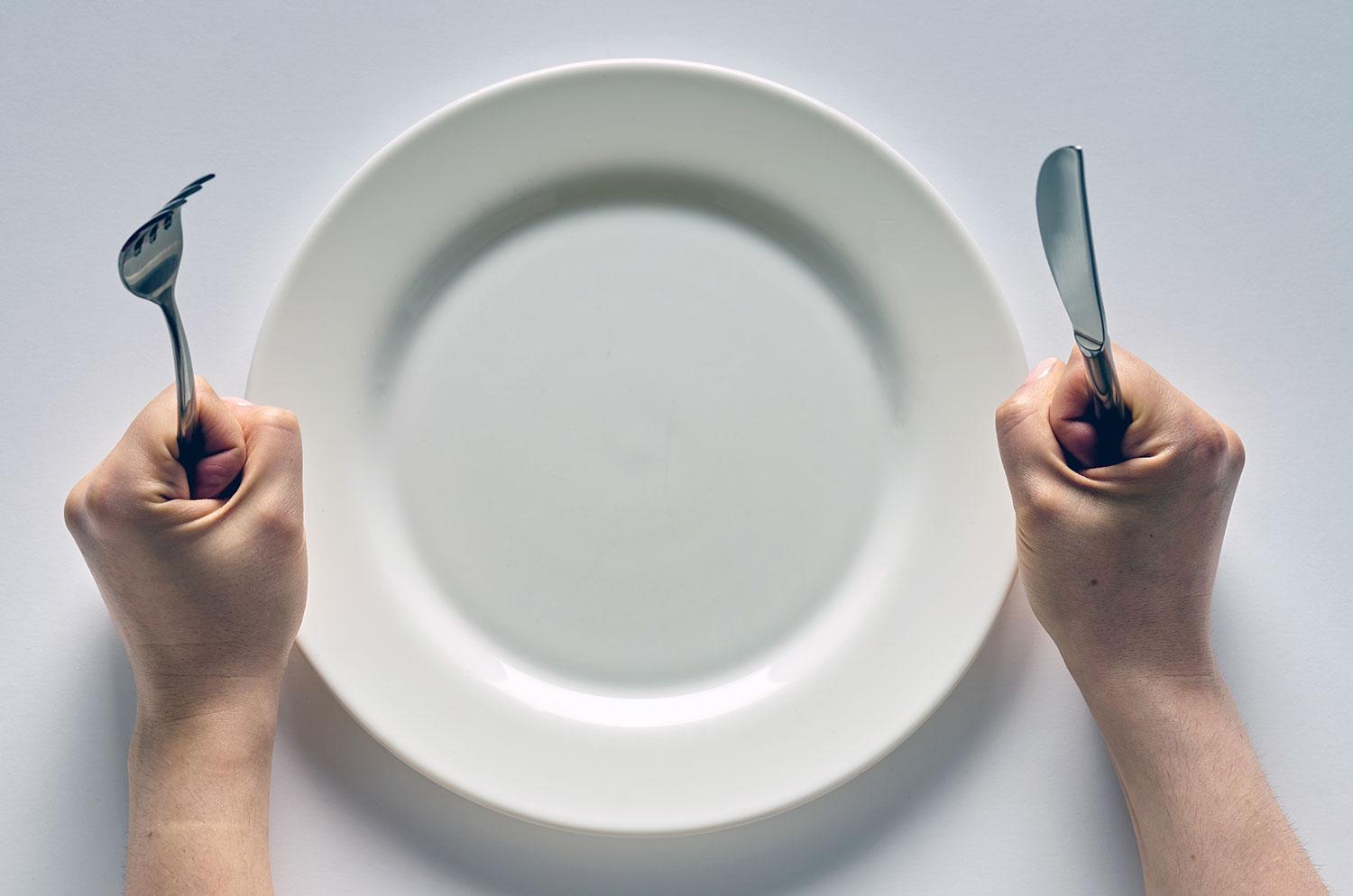 A man holding a knife and fork next to an empty plate
