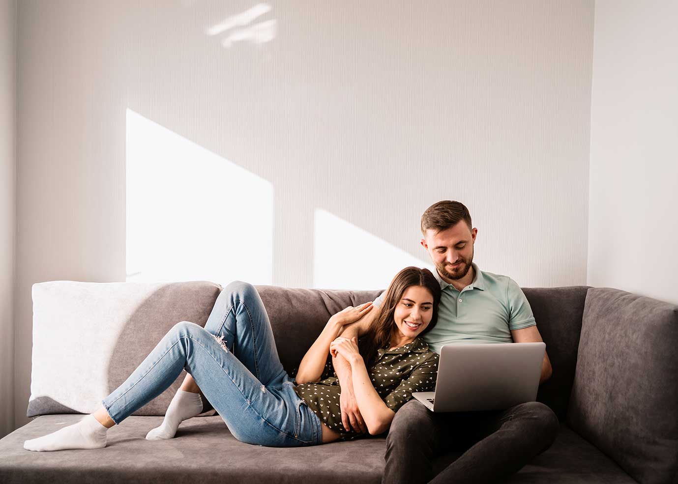 A smiling couple on a sofa looking at a laptop